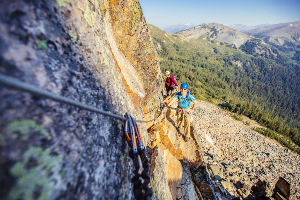 Two climbers stand in the sun on a ledge while climbing the Skyladder via ferrata at CMH Bugaboos.