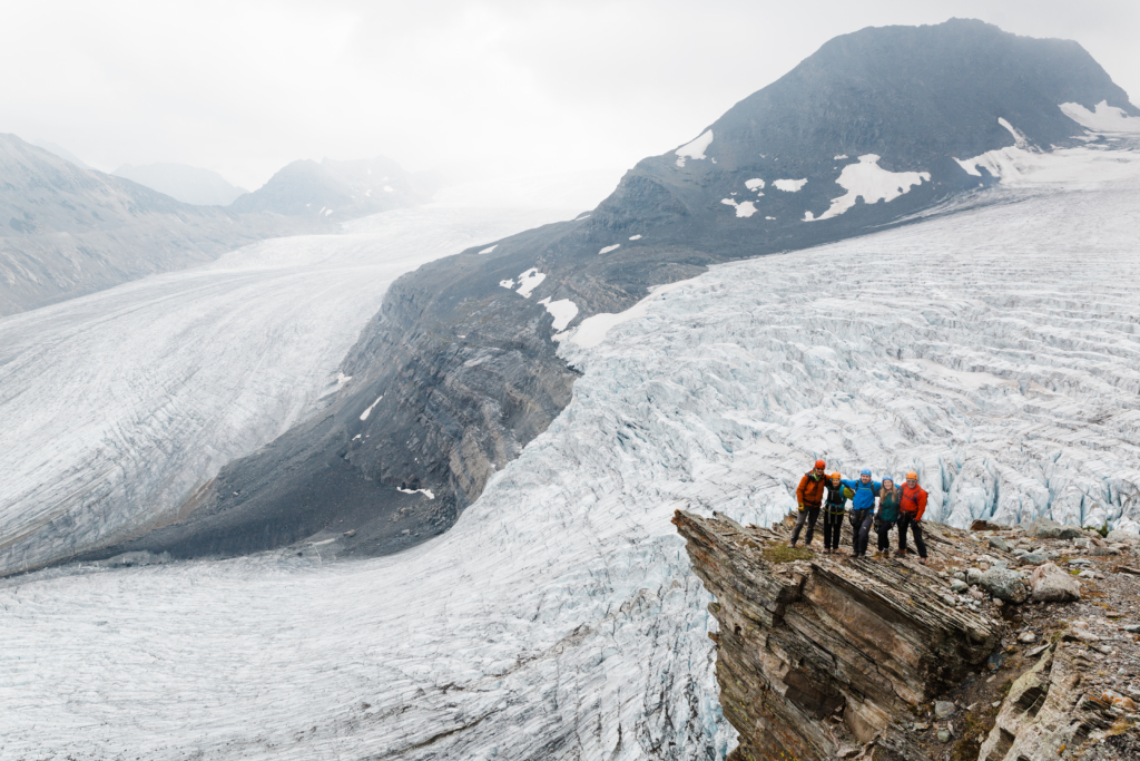 A group of climbers smile at the camera while overlooking a huge glacier at CMH Bobbie Burns.