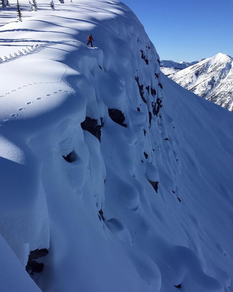 A skier stands on top of a steep cliff ready to ski down