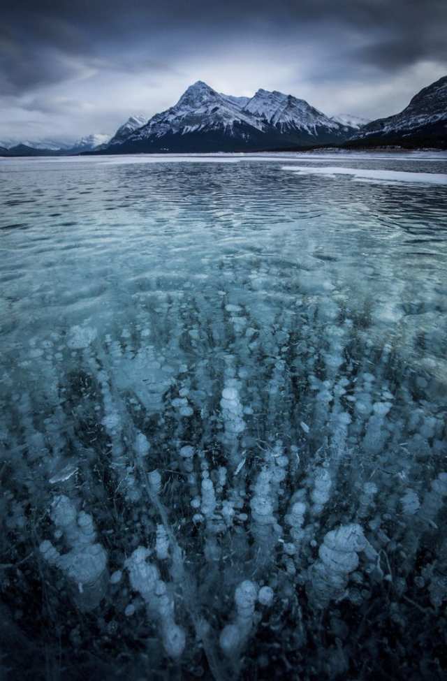 A frozen lake with bubbles below a mountain near the Icefields Parkway