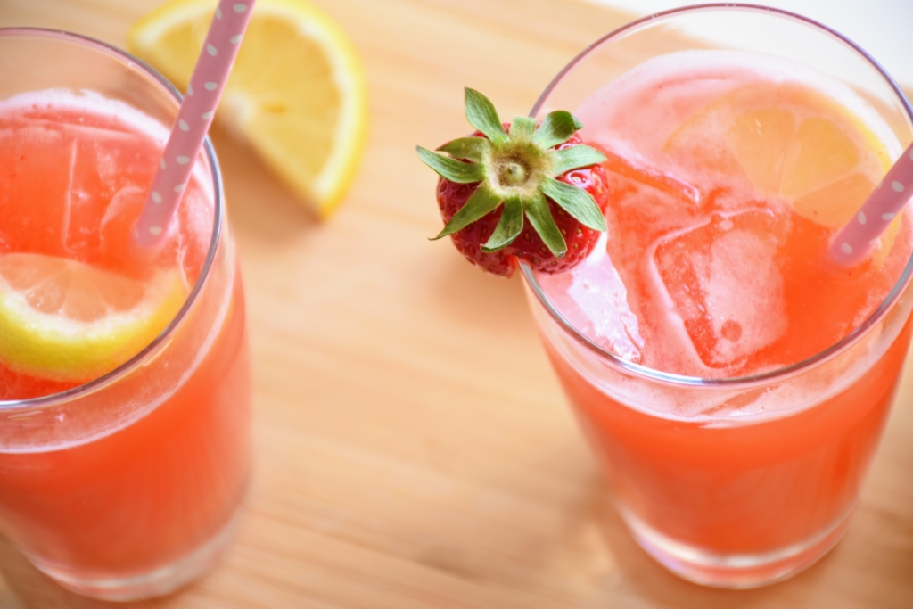 Two peach-coloured cocktails sit on a table, each with a lemon and strawberry as a garnish
