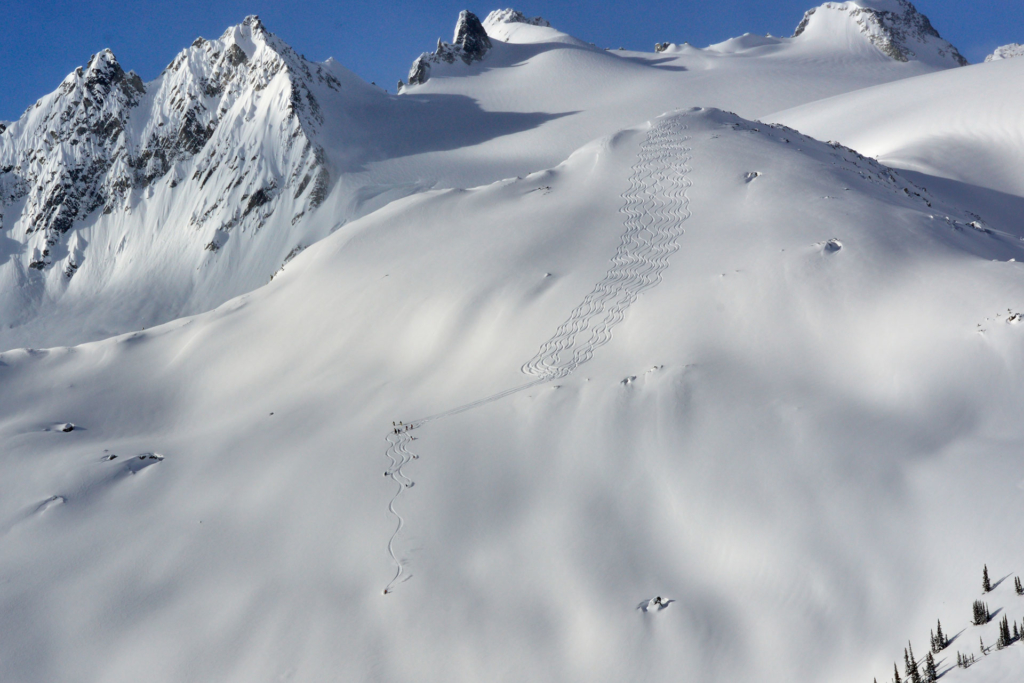 CMH heli-skiing guests skiing in a classic flying v pattern down a glaciated slope. 