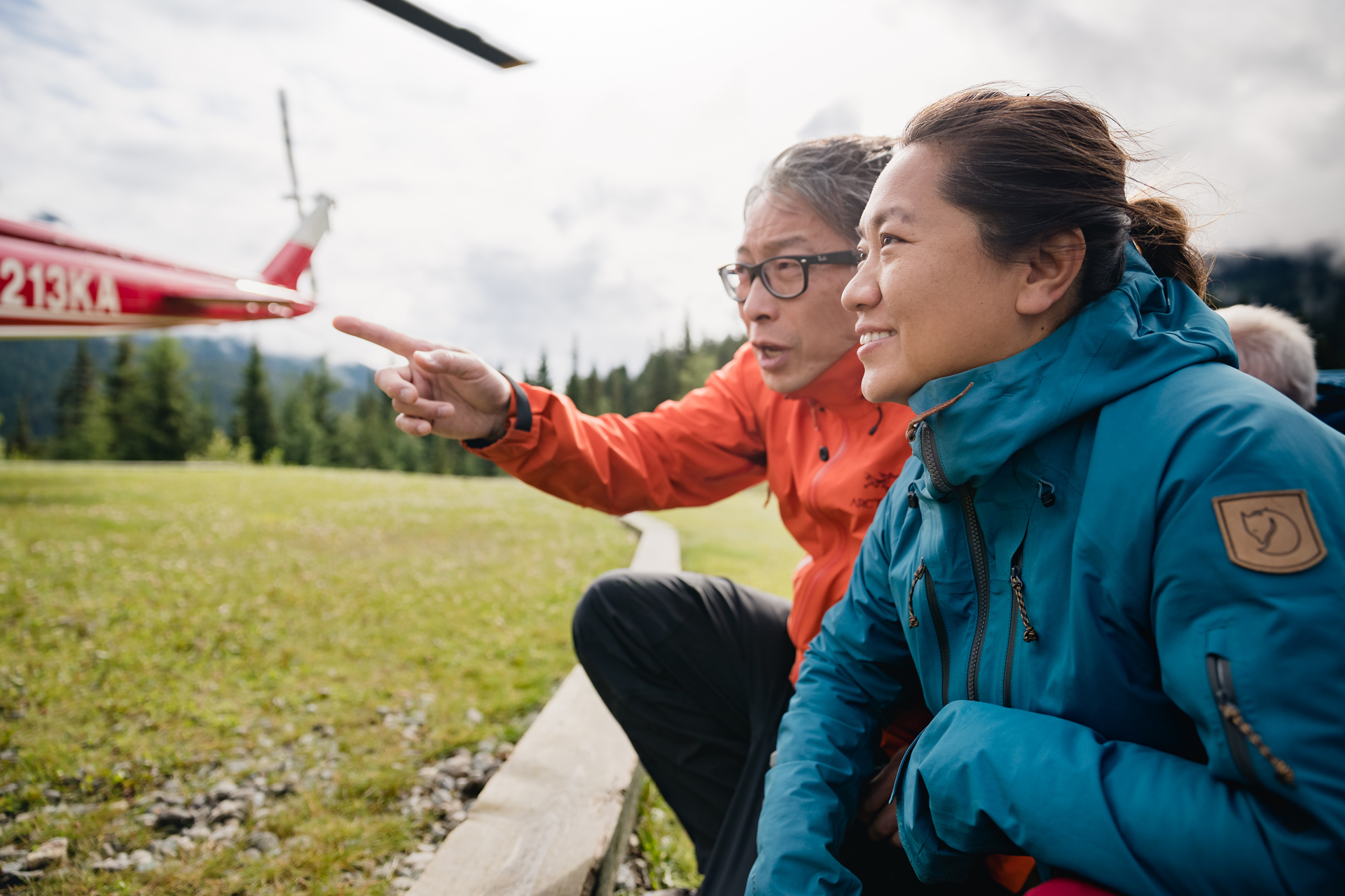 An adult couple crouched beside a landed helicopter. 