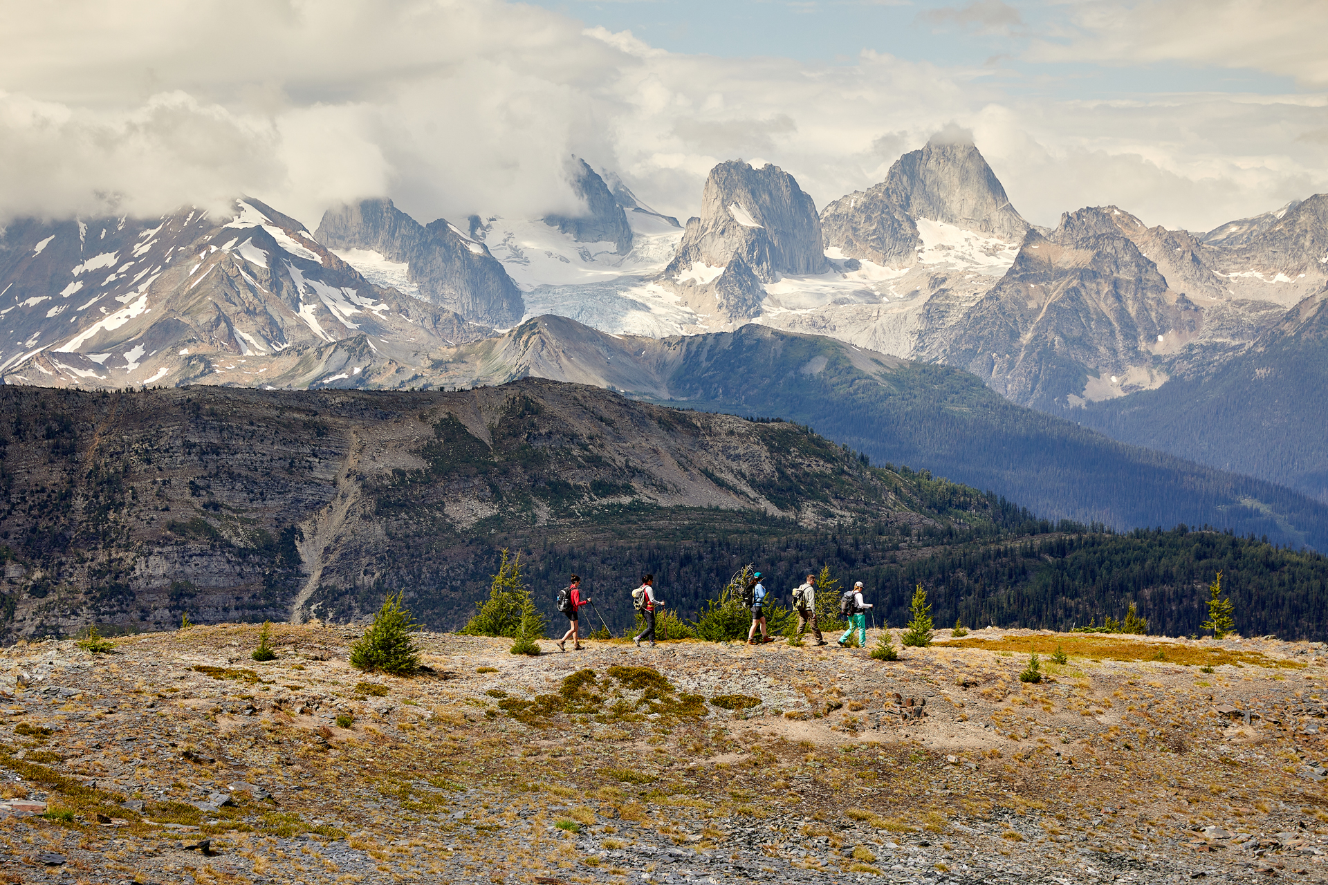 A group of hikers traversing a ridge in front of an epic mountain setting. 