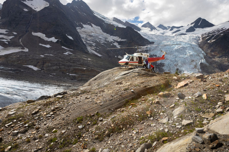 A helicopter landed on a remote perch in front of a glacier.