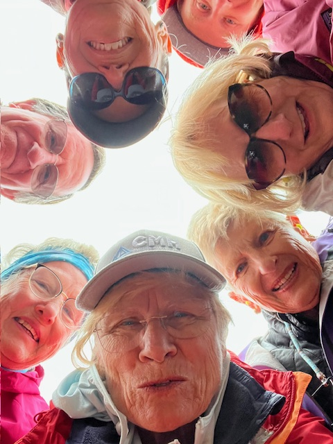 A bunch of female hikers smiling and looking down at the camera.