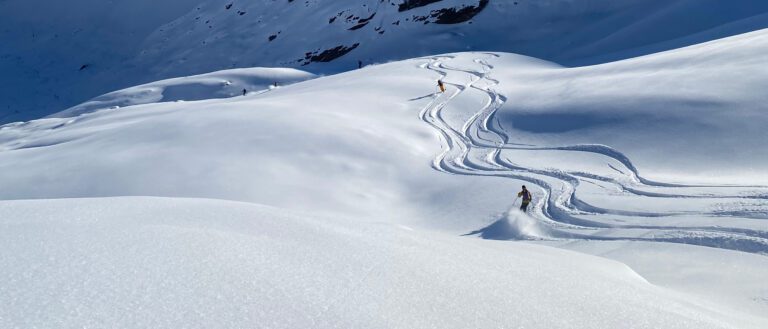 Two skiers making fresh tracks on a wide, untouched snow-covered slope at CMH